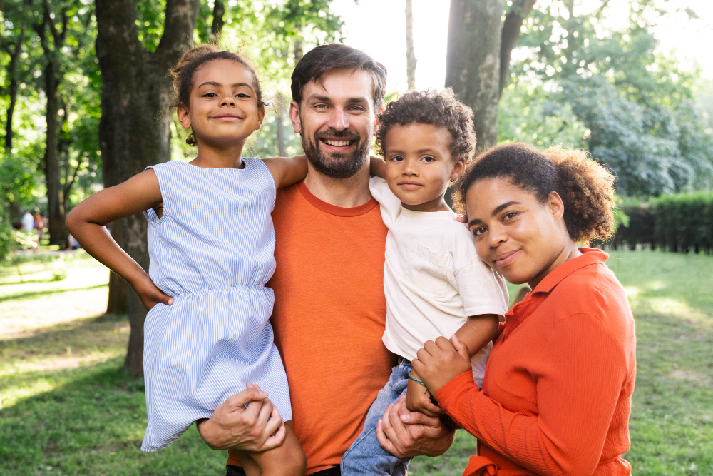 Couple avec jeunes enfants dans un parc qui sourient face à l'objectif.