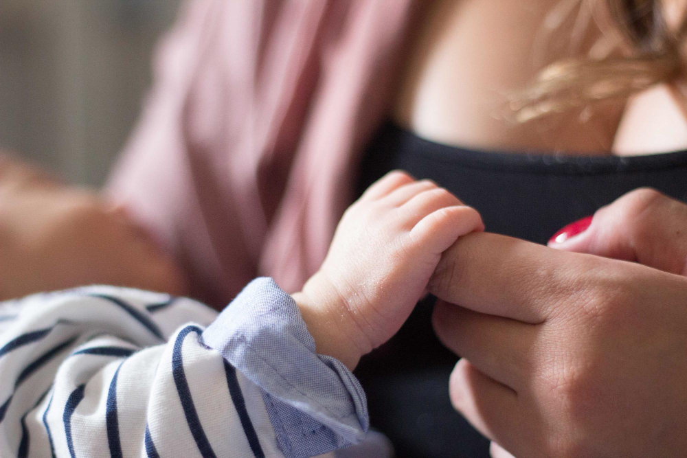 Gros plan sur la main d'un bébé qui tient le doigt de sa maman.