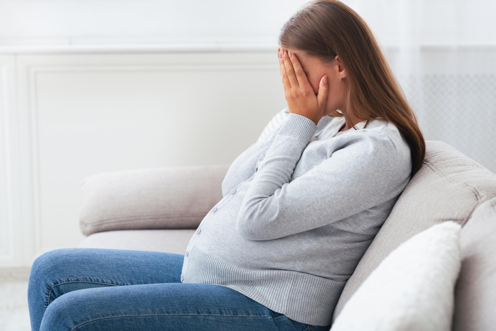 Femme enceinte pleurant et couvrant son visage avec les mains.