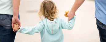 Petite fille de dos qui tient la main de ses parents.