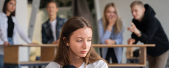 Jeune fille en avant-plan triste et en arrière-plan jeunes qui rigolent.